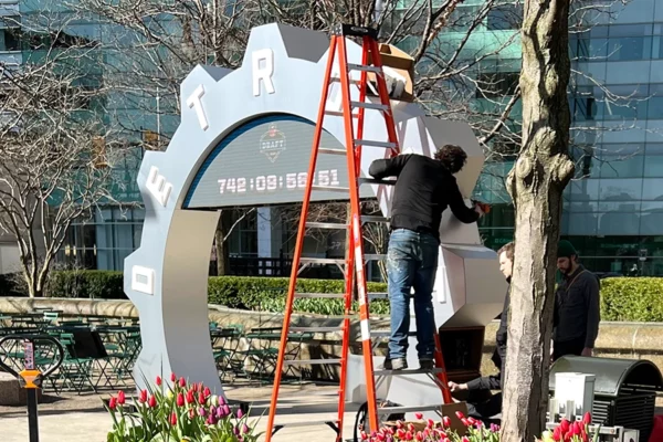 Crew member on a ladder installing the NFL Draft countdown clock at Campus Martius Detroit