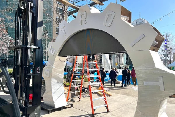 Forklift and crew installing the NFL Draft countdown clock structure at Campus Martius with ladders and scaffolding