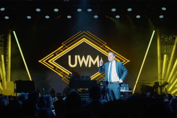 Presenter on stage at UWM 2022 holiday party with gold branding
