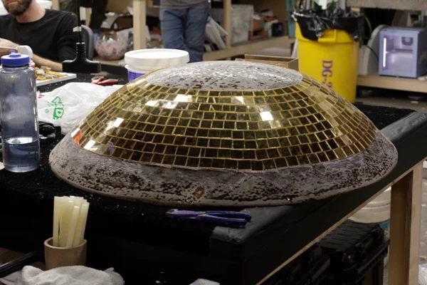 Gold mirror tile section applied to football dome prop in fabrication