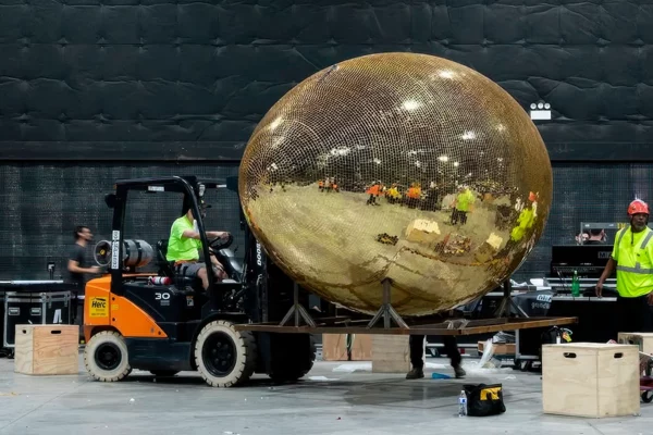 Forklift positioning gold mirror football sculpture on venue floor