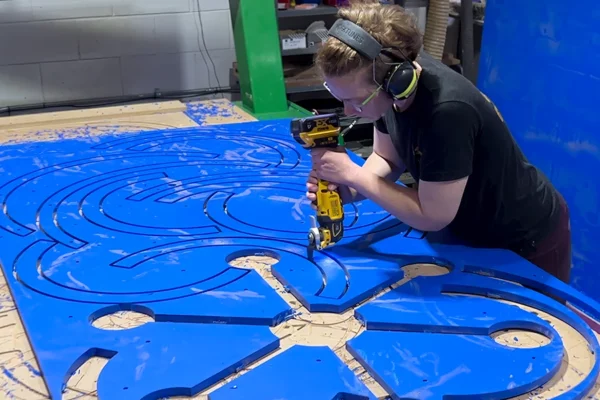 Display Group crew member drilling blue sculptural panel on shop floor