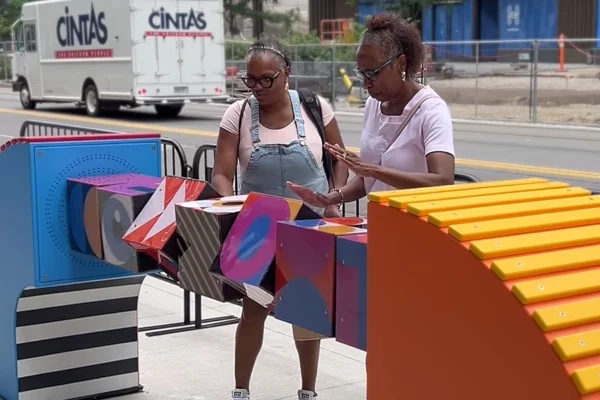 Two women interacting with Bedrock streetscape interactive sculpture panels